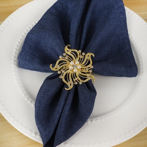 Portatovagliolo a fiore dorato con perle e cristalli su tovagliolo di lino blu e piatto