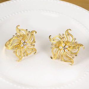 Portatovaglioli a forma di fiore dorato con perle e strass su un vassoio di ceramica bianca