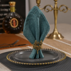 Elegant gold coral branch napkin ring with dark green napkin on a ceramic plate