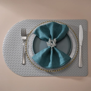 Close-up of silver coral branch napkin ring with dark green fabric on grey woven mat