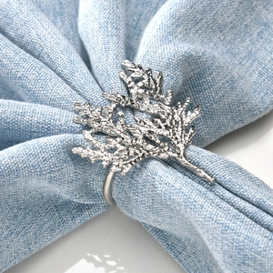 Detailed close-up of a silver coral branch napkin ring on light blue linen fabric