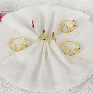 Set of 4 gold Eid metal napkin rings on a white napkin with a minimalist festive table setting