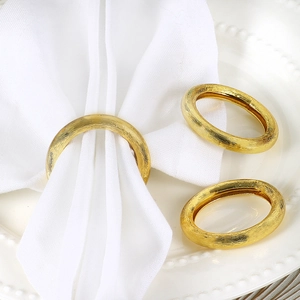 Modern gold round napkin ring with brushed metal texture on a white cloth napkin