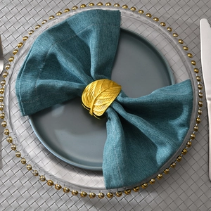 Golden metal leaf napkin ring with detailed vein texture on a dark blue cloth