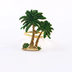 Close-up of golden metal napkin ring featuring green enamel palm trees on white backdrop