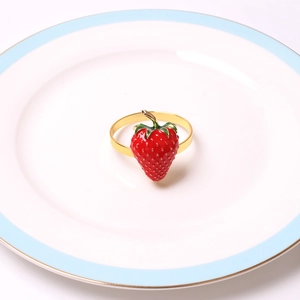 Dettaglio portatovagliolo a forma di fragola in smalto rosso con base dorata su piatto