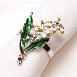 Détail d'un rond de serviette en émail muguet blanc et jaune sur tissu blanc doux