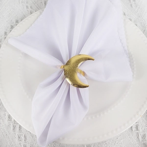 Detail of gold crescent moon napkin ring with frosted texture on white table setting