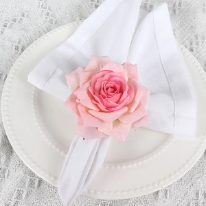 Close-up of pink artificial rose napkin ring on white fabric for wedding table decor