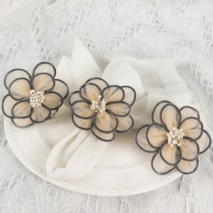 Three champagne mesh flower napkin rings with pearls on white lace tablecloth