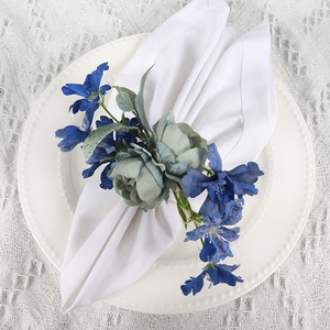 Deep blue faux rose napkin ring with green leaves on white linen napkin on a plate