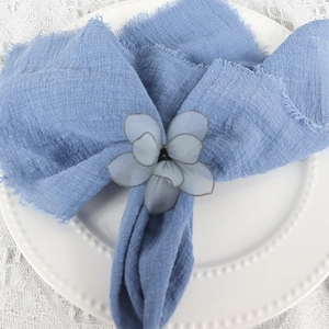 Detail of gray-blue mesh flower napkin ring on blue linen fabric and white ceramic plate
