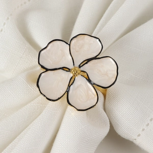 Elegant gold flower napkin ring with cream white petals and black edges on linen