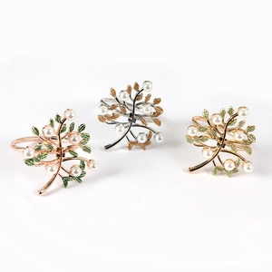 Detailed view of three metal napkin rings featuring tree designs and white pearls