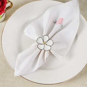White five-petal flower napkin ring with gold center on a ceramic plate setting