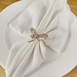 Close-up of golden bow tie napkin ring with rhinestones on a white linen napkin