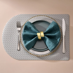 Golden brushed metal napkin ring set with green linen napkin on modern dinner table