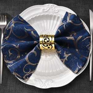 Golden cutout comma napkin ring with dark blue patterned cloth on white plate