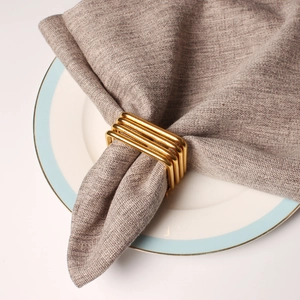 Square gold plated napkin ring with geometric hollow design on linen napkin and white plate
