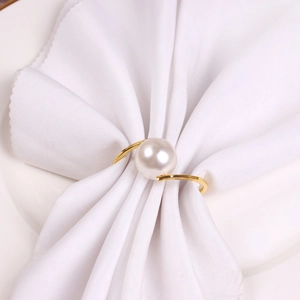 Elegant gold S-shaped metal napkin ring with a large white pearl on a white cloth