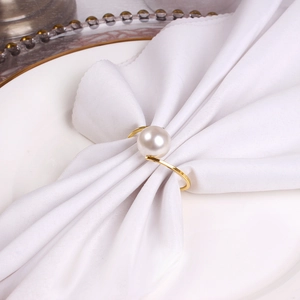 Macro shot of gold-plated napkin ring with a single white pearl on a white napkin