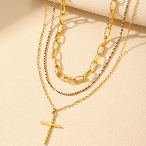Detail view of a layered gold necklace featuring a classic cross pendant and box chains