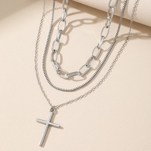 Three-layer silver cross pendant necklace with box chains on beige leather background