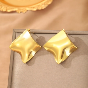 Warm gold stainless steel wavy geometric earrings hanging on a luxury jewelry box edge