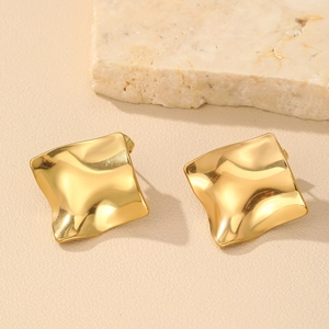 Detailed macro view of gold ripple textured square stud earrings on marble stone