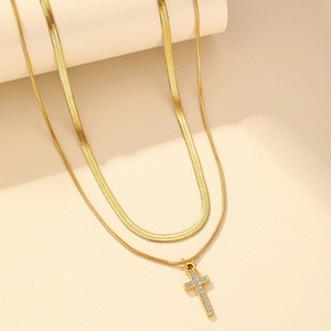 Detail of a double-layered gold necklace with a herringbone chain and cross pendant