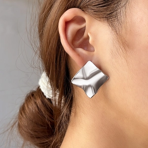 Close-up of square silver stainless steel earrings with wavy textured surface on model