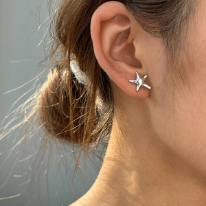 Gros plan d'une boucle d'oreille étoile de mer en argent portée avec reflets naturels