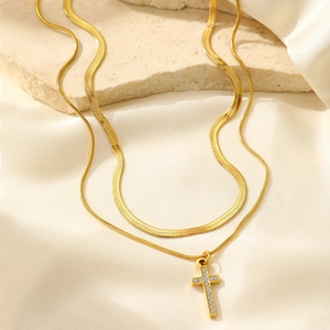 Detail of layered gold snake chain and rhinestone cross pendant on silk background