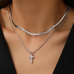Close-up of double-layered silver necklace featuring a crystal cross pendant and snake chain