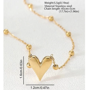 Detail of a polished gold heart pendant with a small bead chain on a textured fabric background