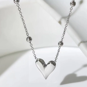 Macro detail of silver heart pendant with beaded chain on minimalist white stand