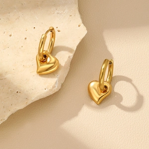 Détail de boucles d'oreilles cœur en or poli sur une surface de pierre texturée