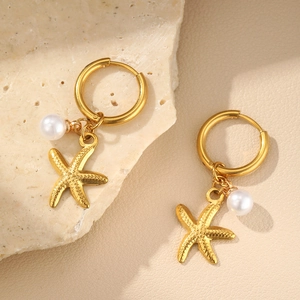 Detail of gold starfish earrings with white pearl pendants on textured stone background