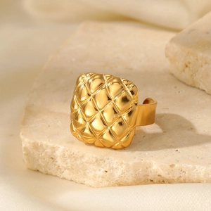 Detailed close-up of a gold ring with geometric square textures on a natural stone base