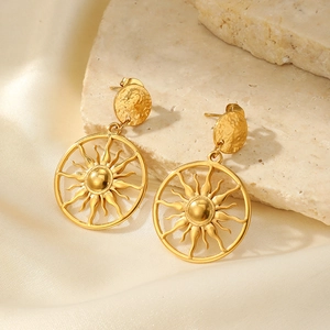 Détail de boucles d'oreilles soleil avec texture martelée sur pierre et soie crème