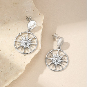 Boucles d'oreilles soleil argentées avec texture martelée sur un fond de pierre neutre