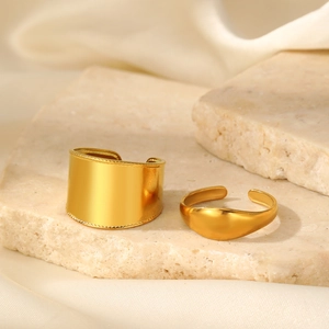 Dettaglio di anelli placcati oro opaco minimalisti su pietra beige e seta