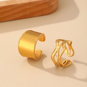Detailed shot of double-layered twist and wide gold rings on a textured beige backdrop
