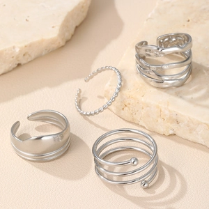 Detail view of four irregular silver stackable rings on beige travertine background