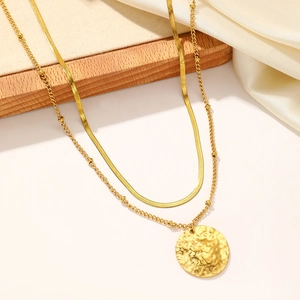 Close-up of golden double-layer chain with hammered circular pendant on silk fabric