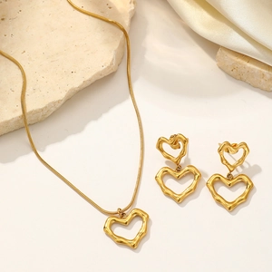 Parure de bijoux dorés avec collier et boucles d'oreilles cœur sur tissu satiné