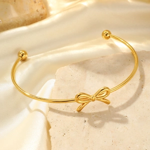 Elegant gold bow-shaped open bangle with adjustable knot design on marble and silk background