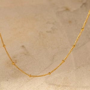 Gros plan d'un collier ras du cou minimaliste à billes dorées sur marbre chic