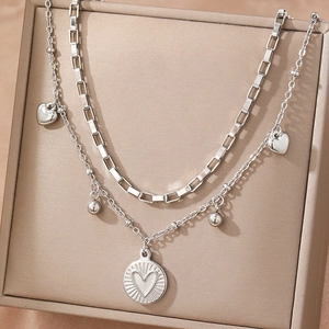 Double-layered silver necklace with heart charms and polished disc on a jewelry box