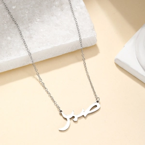Arabic script name necklace in 18K gold titanium steel on an elegant stone display